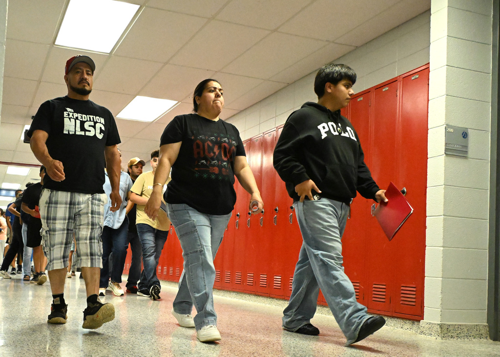 three people in black tops walking in a high school hallway
