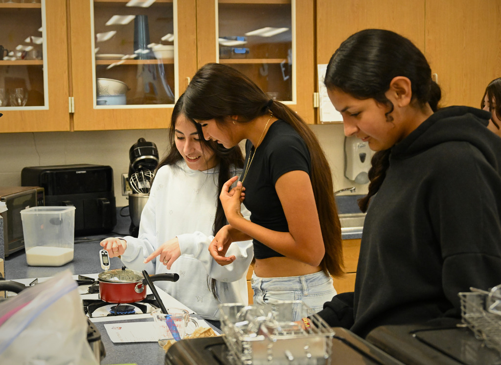 three students cooking in a kitchen
