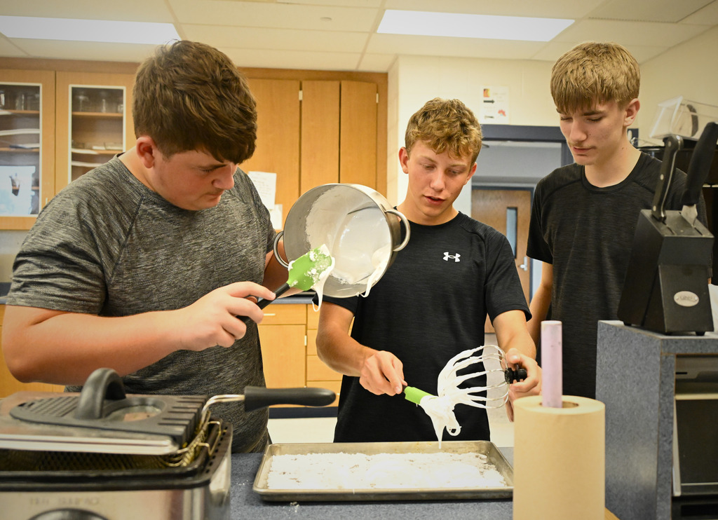 three students cooking in a kitchen