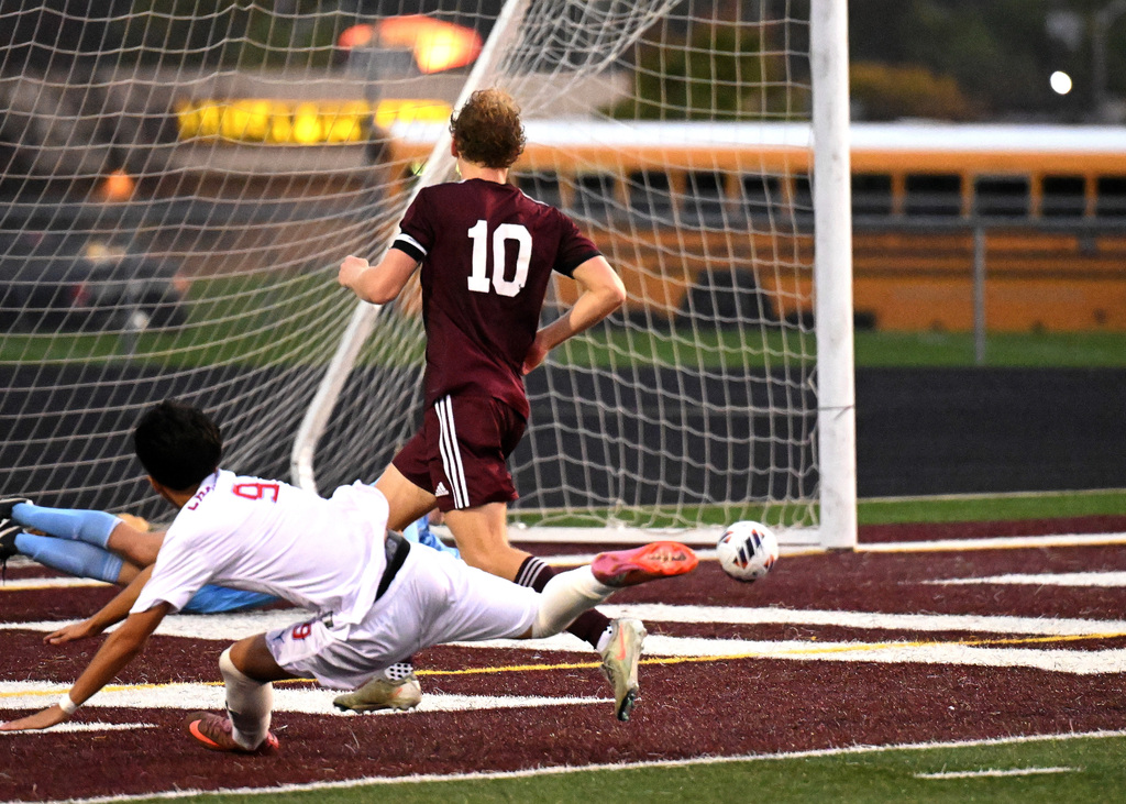a soccer player kicking the ball into the net with two defenders chasing