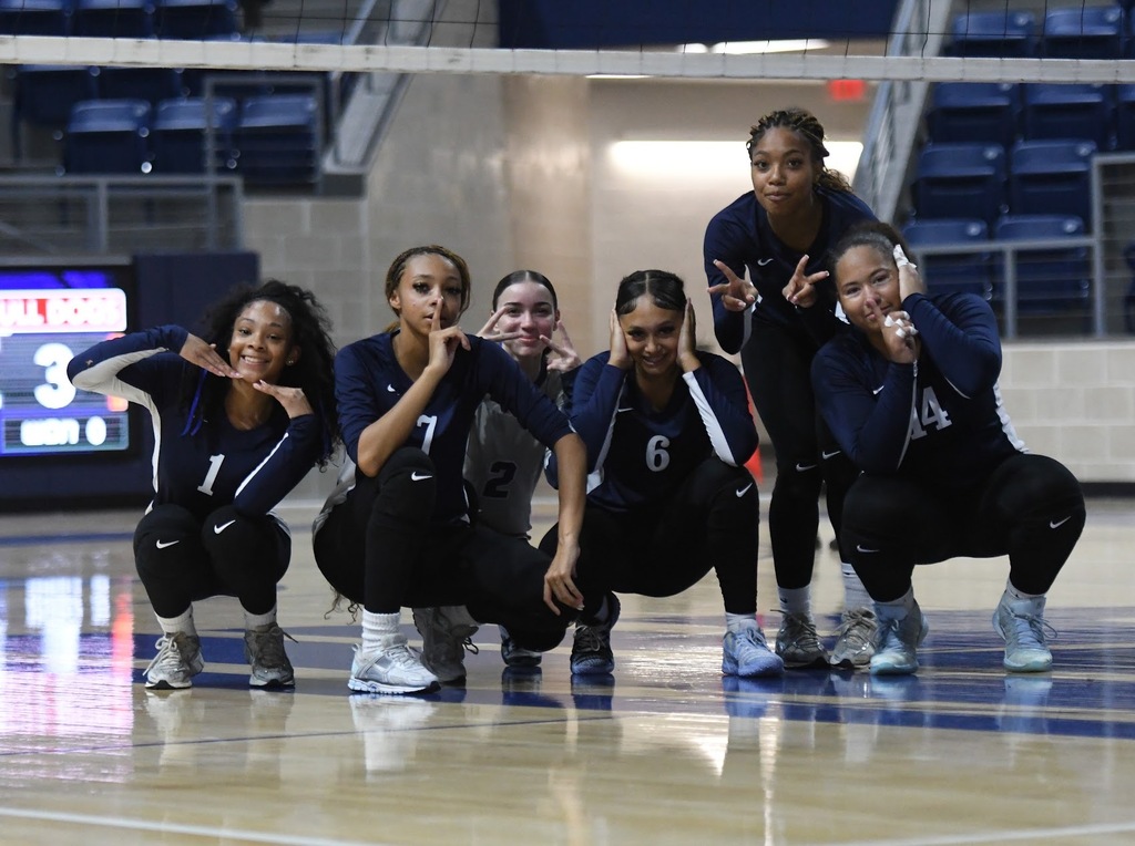 WOS volleyball players squatting and posing under the net