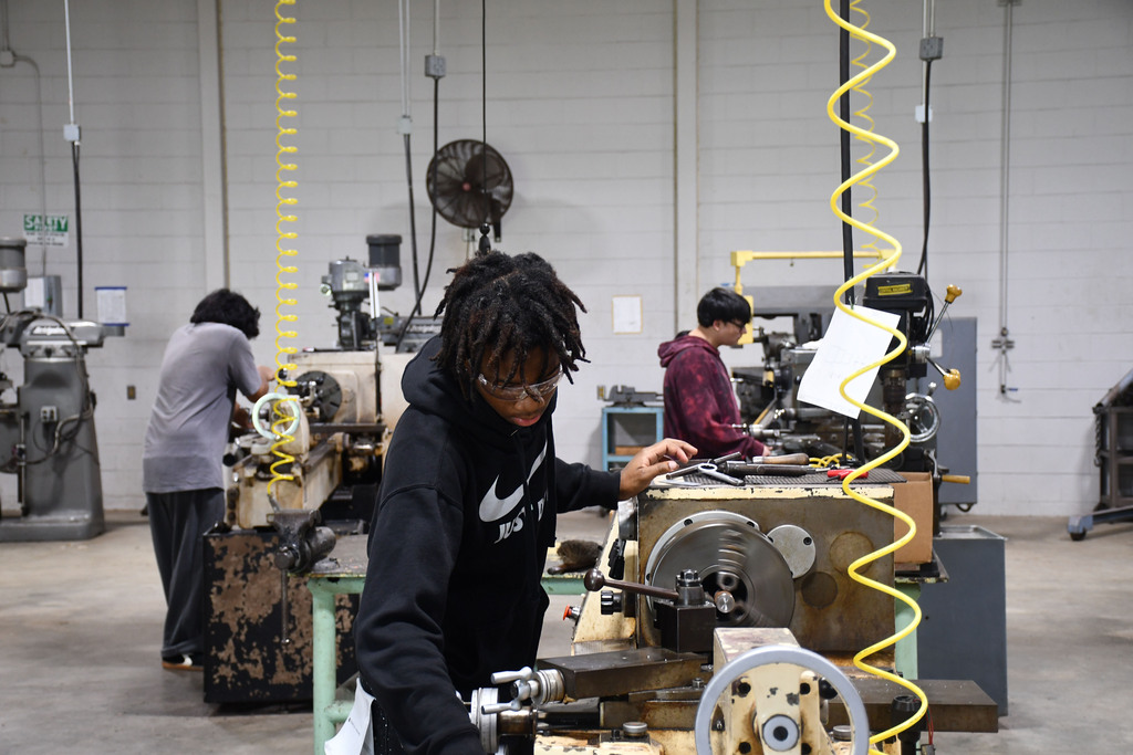 Three students are operating different machines in class