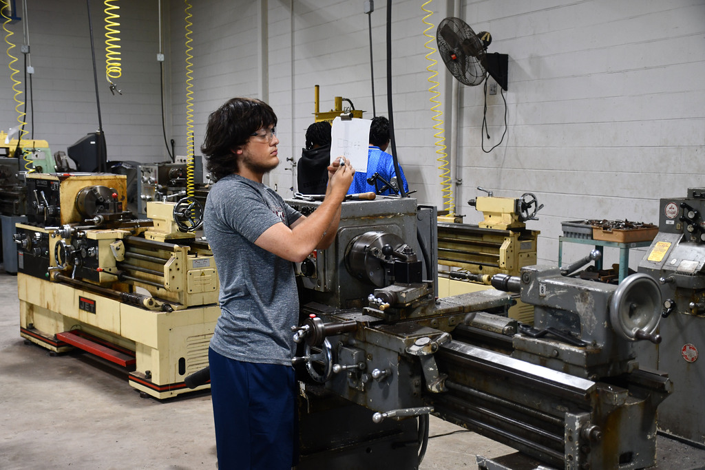Young man in gray t-shirt examining a machine piece