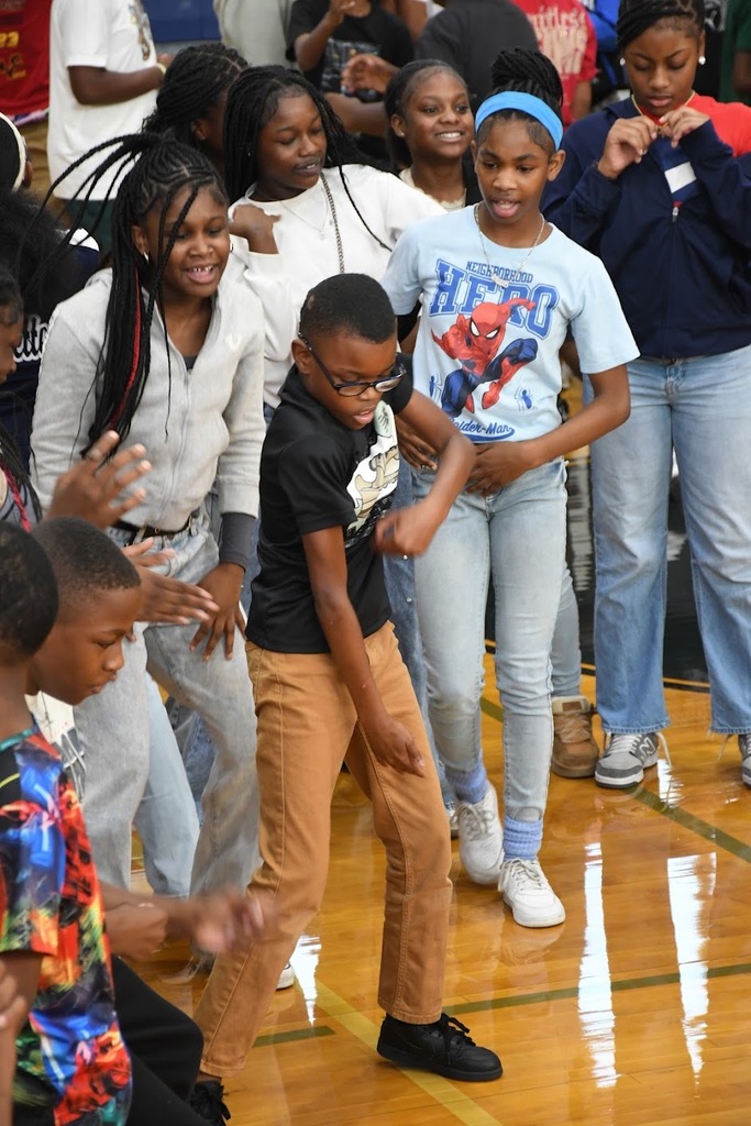 a boy doing a dance move in front of a crowd of students