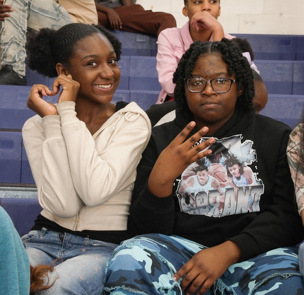 two students posing for the camera, one making a heart with her hands, another holding up a W with their fingers.