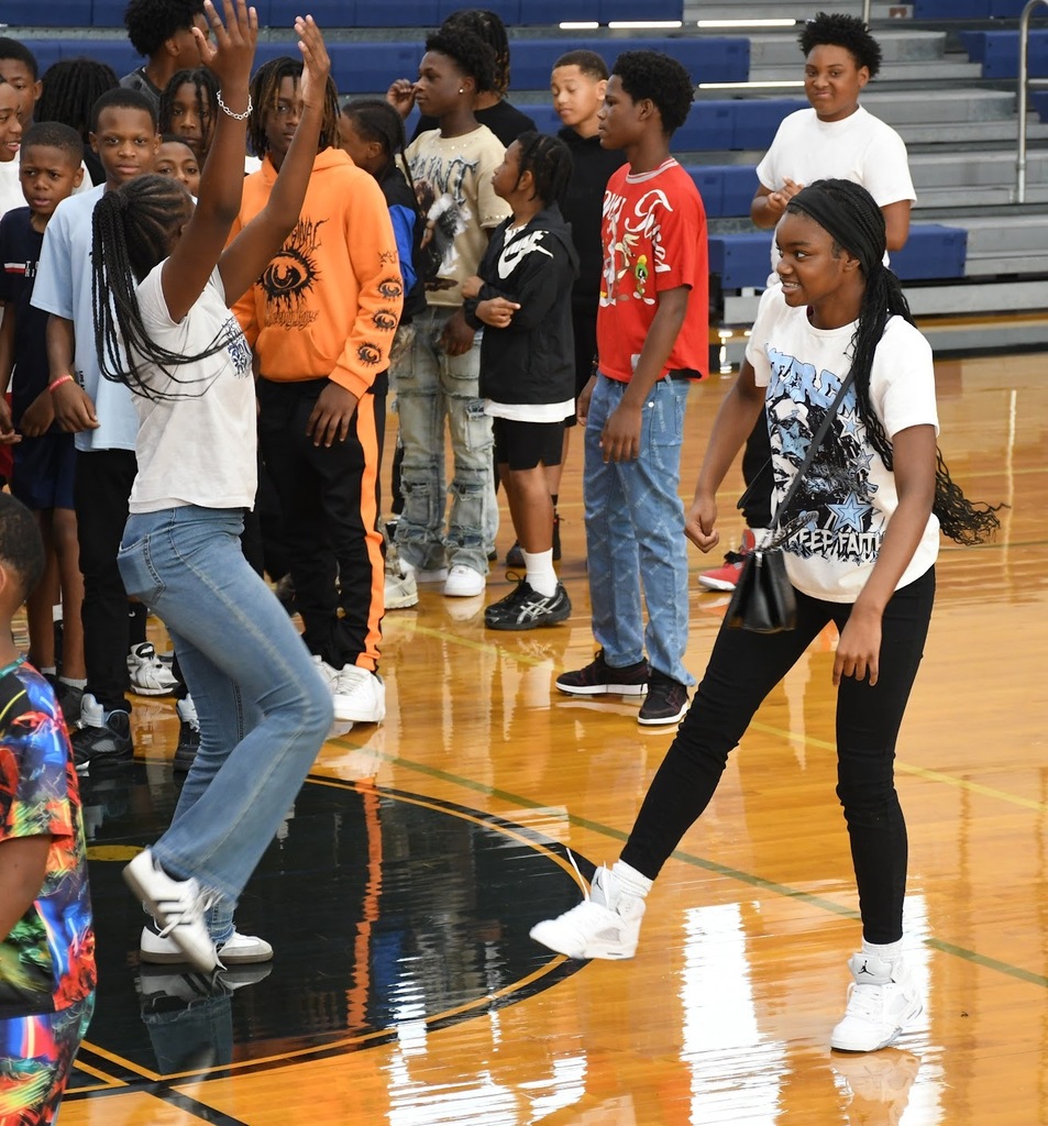 two girls in the gym dancing in front of a large group of students