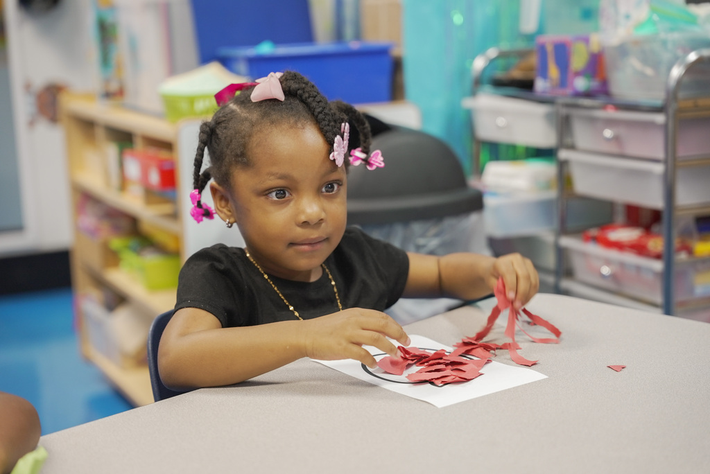 girl putting red strips of paper on an apple outline