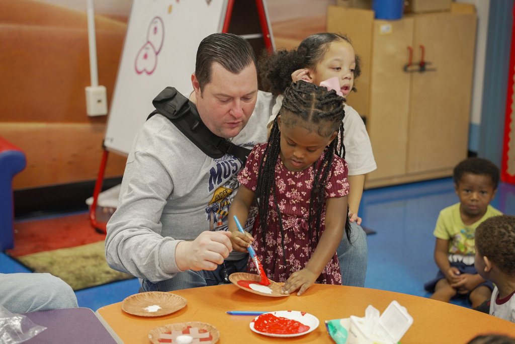 teacher helping girl paint a paper plate with red "pie filling"