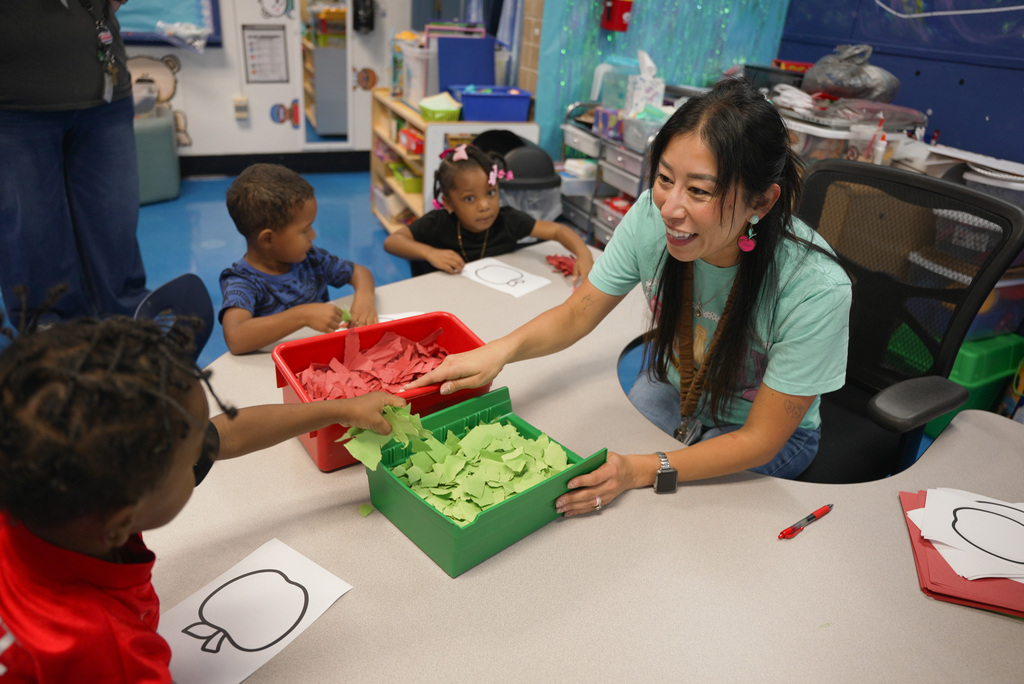 a teacher handing out scraps of red and green paper for an apple project