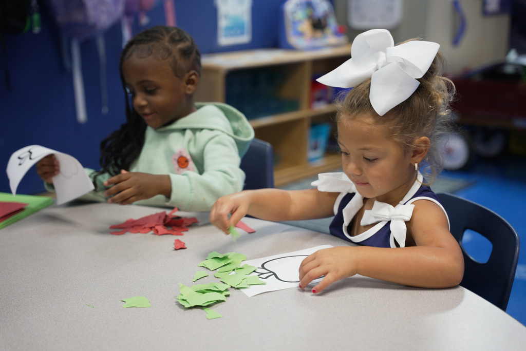 two girls placing red and green strips of paper on their cutout to make an apple