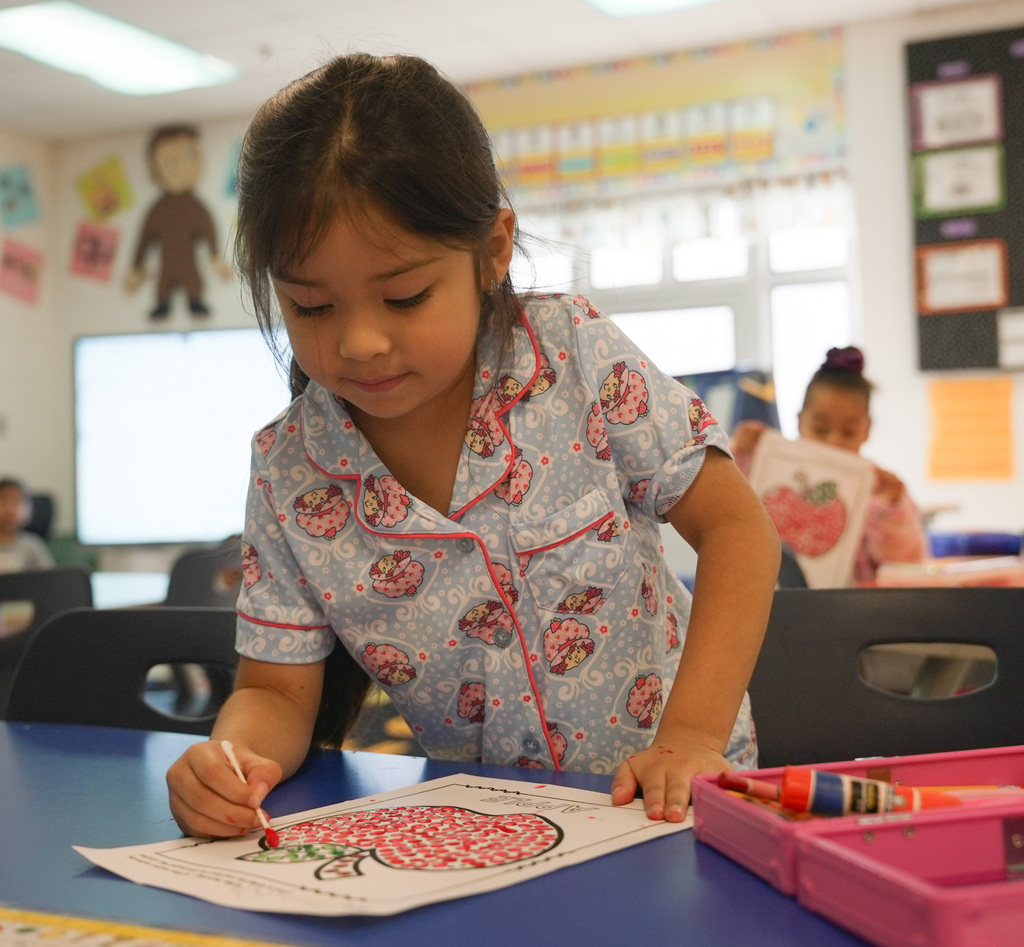 girl leaning over her worksheet to color an apple