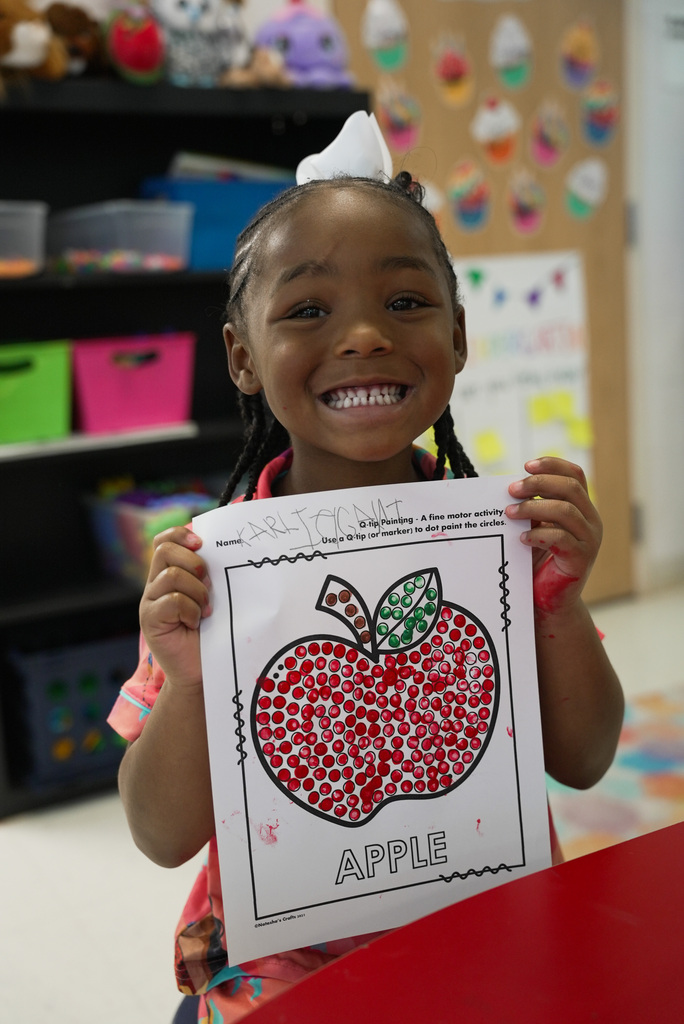 girl smiling while holding up ger apple coloring worksheet