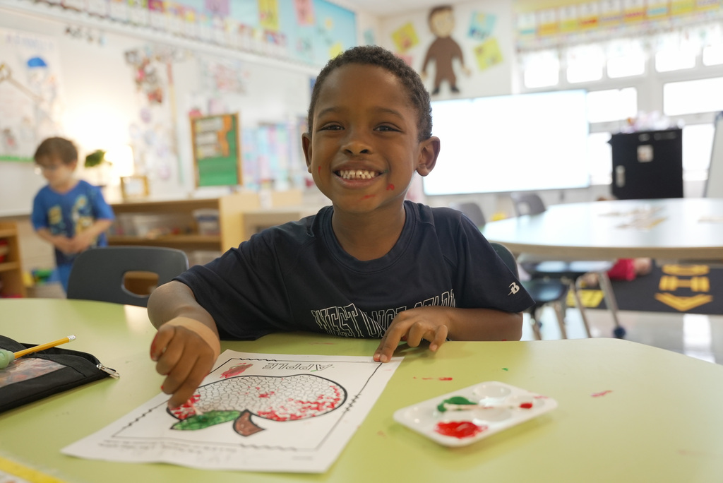 boy smiling while coloring his apple coloring worksheet