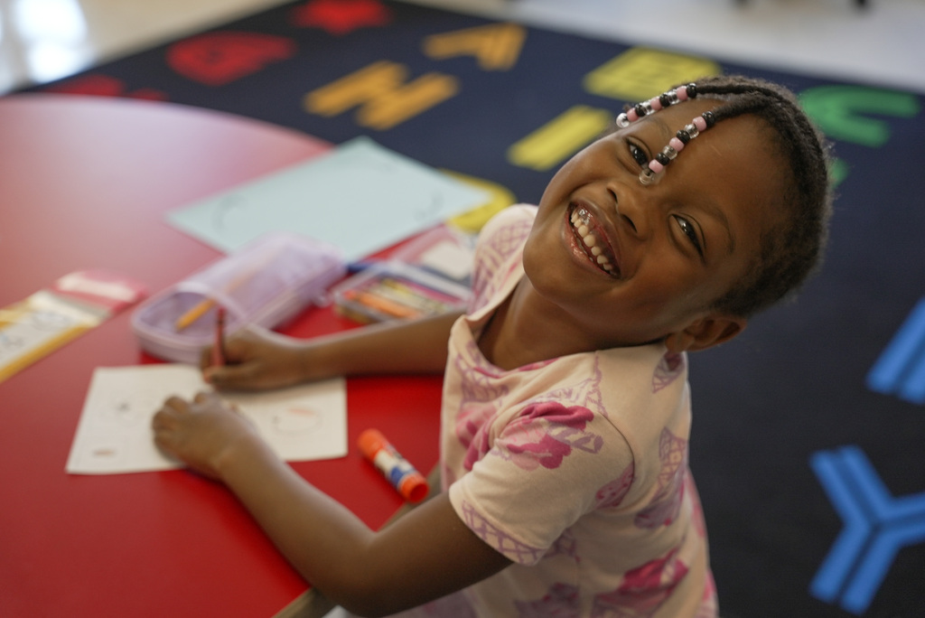 a girl smiles at the camera while working on her worksheet