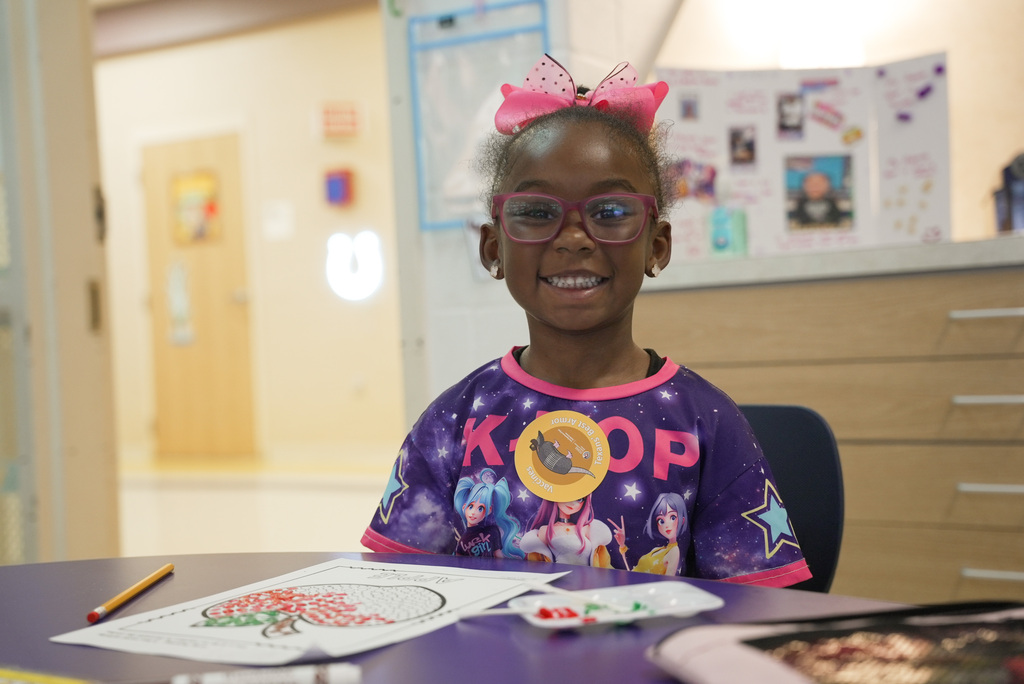 girl smiling at the camera in front of her apple coloring worksheet