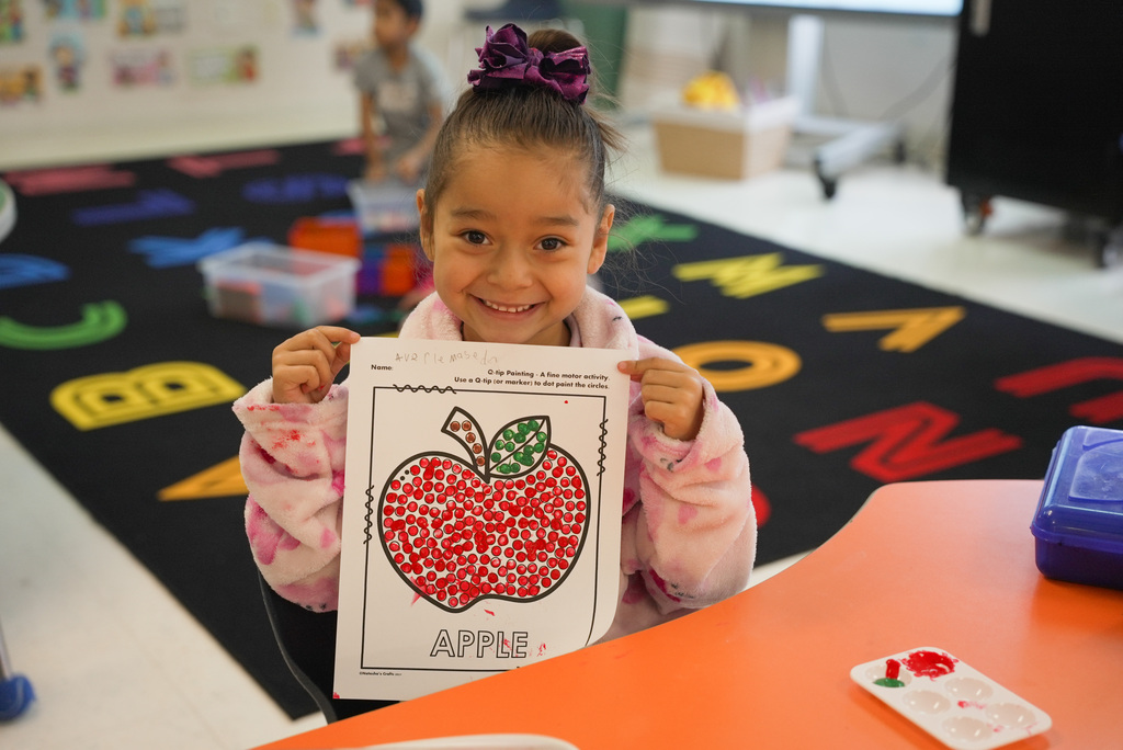 girl smiling while holding up ger apple coloring worksheet