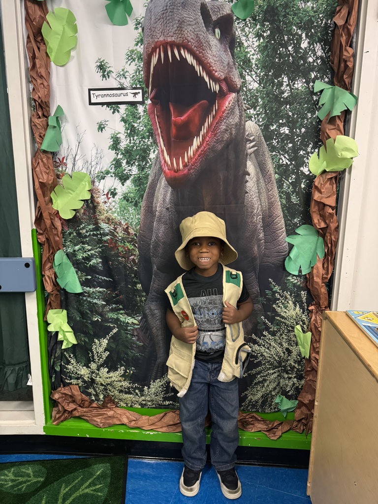 student in safari gear standing in front of a T-Rex poster