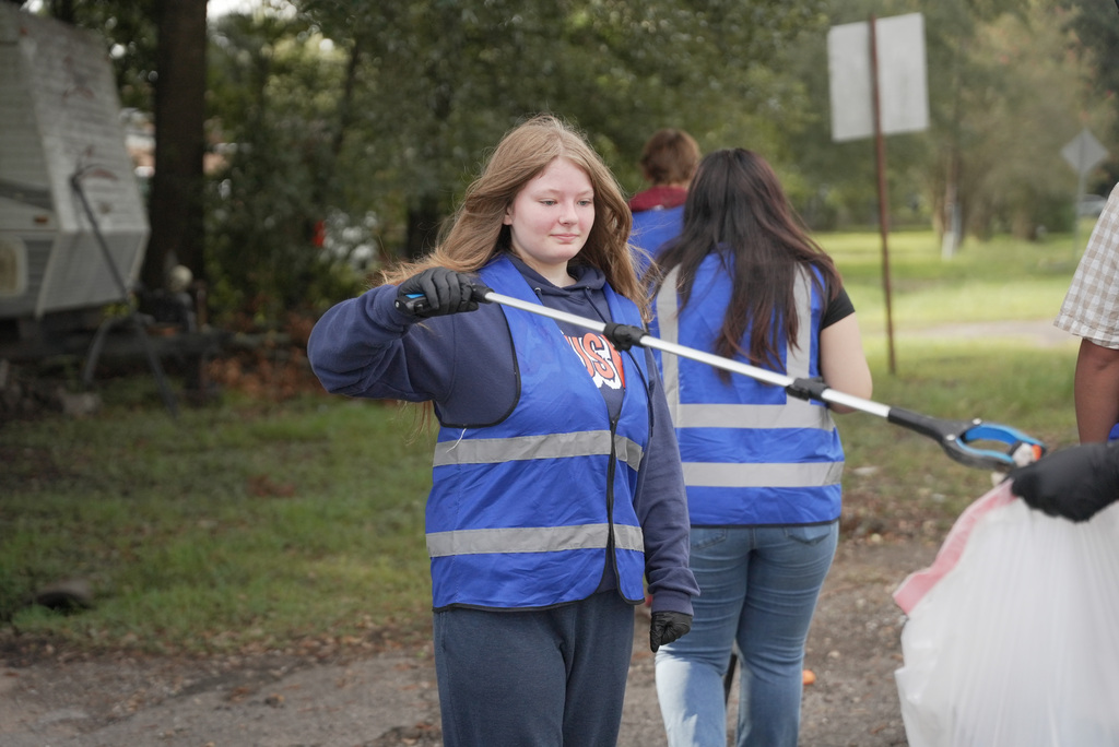 female student using a grabber tool to put trash in a bag