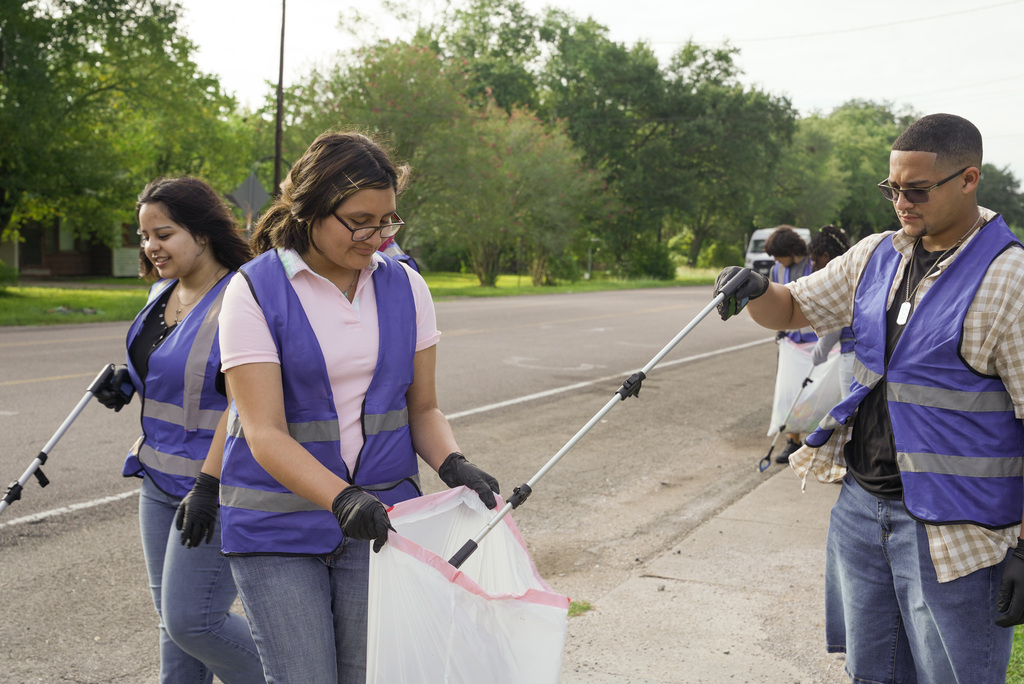 a female student holding a trash bag open as a male student drops trash inside it