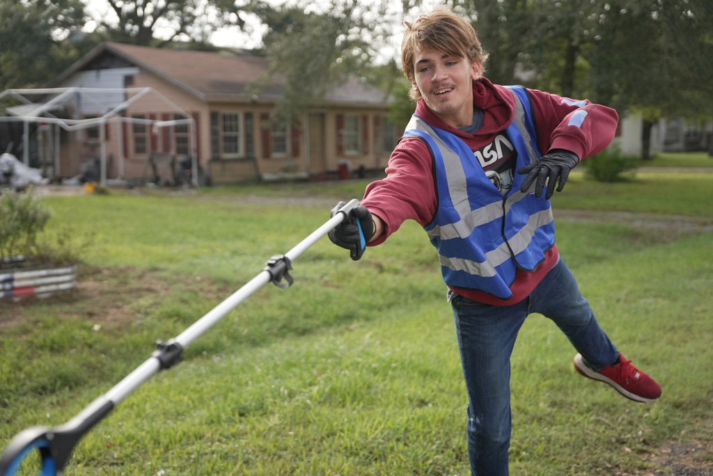 male student leaning over with a grabber tool to deposit trash in bag