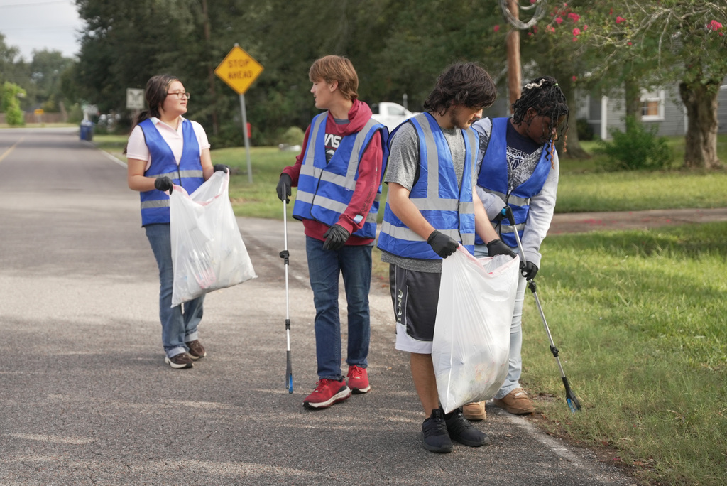 a group of students in blue vests picking up trash on the side of the road