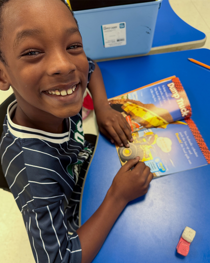 Young boy smiles as reads a book about dump trucks