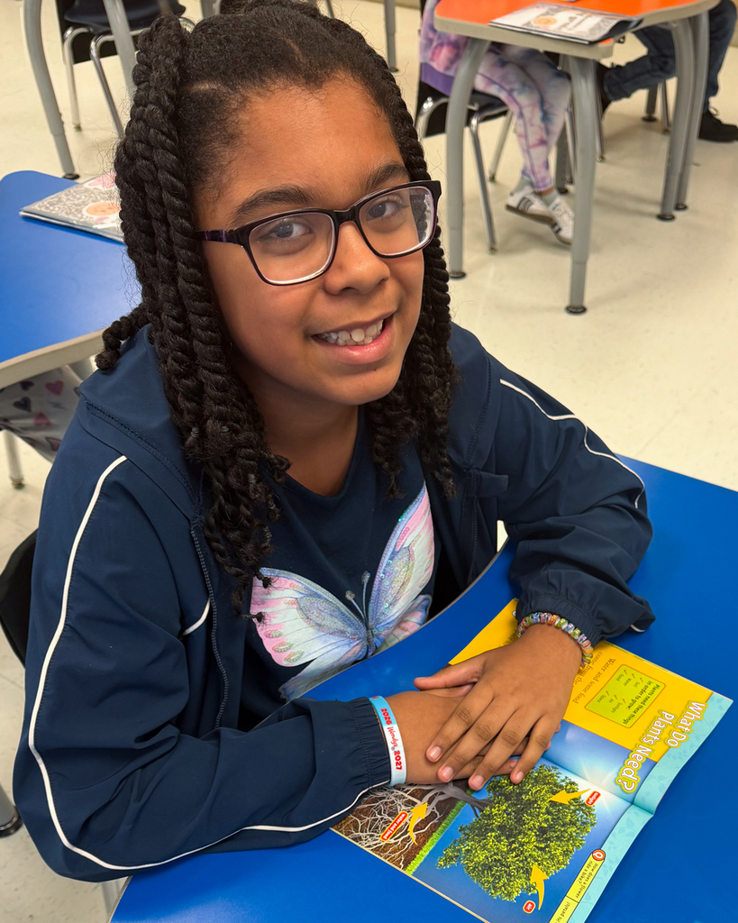 Girl with braided hair and glasses reads a book about trees.
