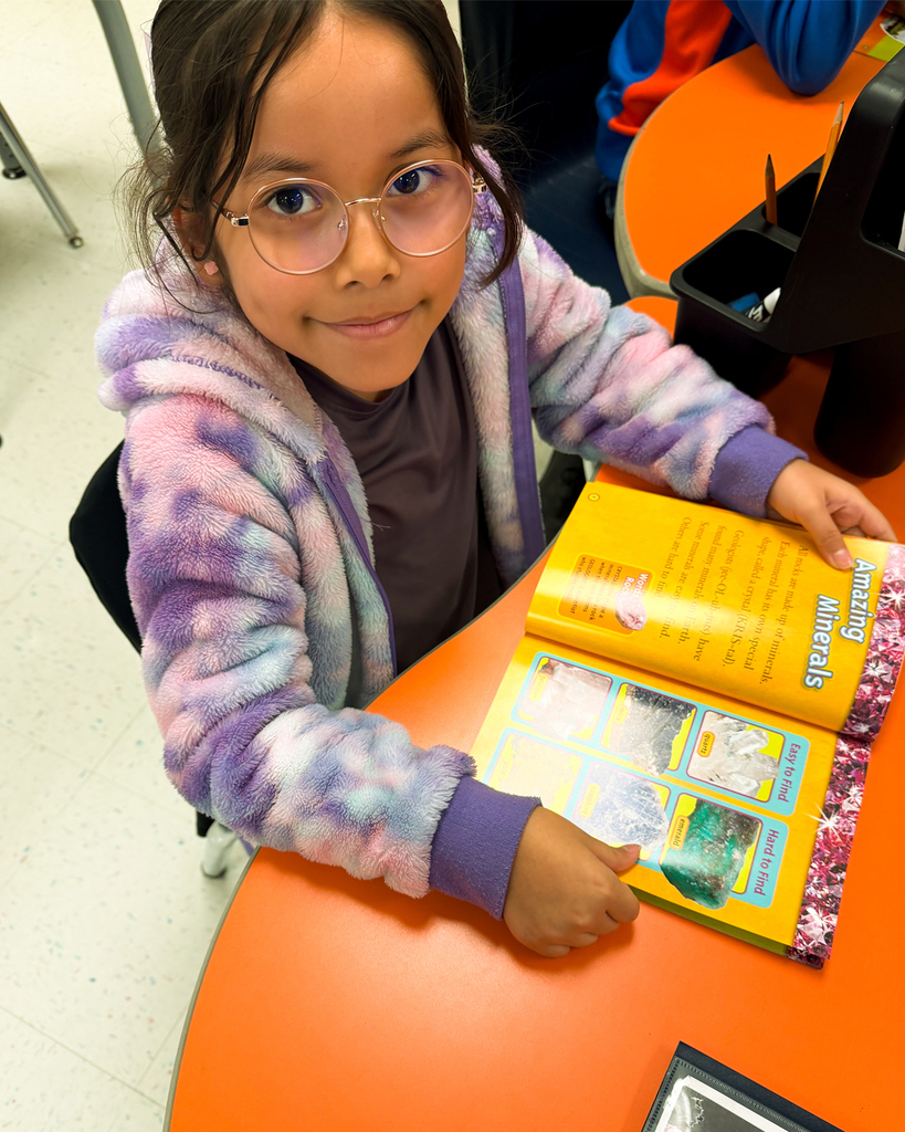 Girl wearing glasses and fuzzy hoodie enjoys a book about minerals