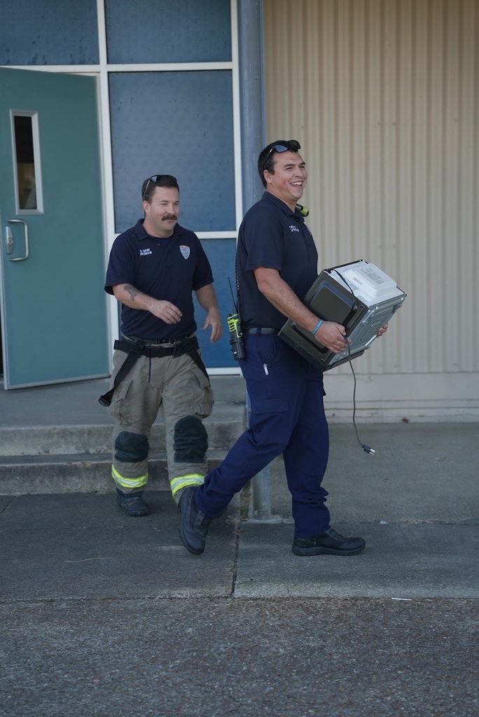 two firefighters walking out a building smiling, with one holding a microwave