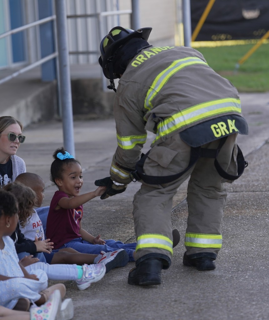 a girl smiling and excited holding hands with a firefighter in full gear