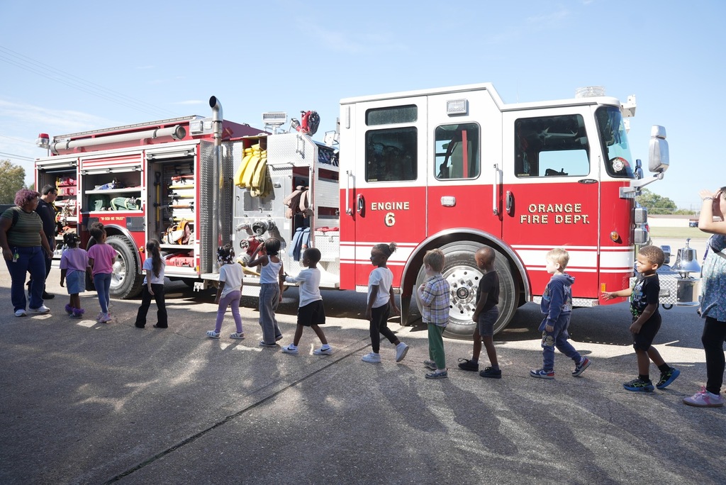 a line of children walking around an Orange Fire Dept. truck