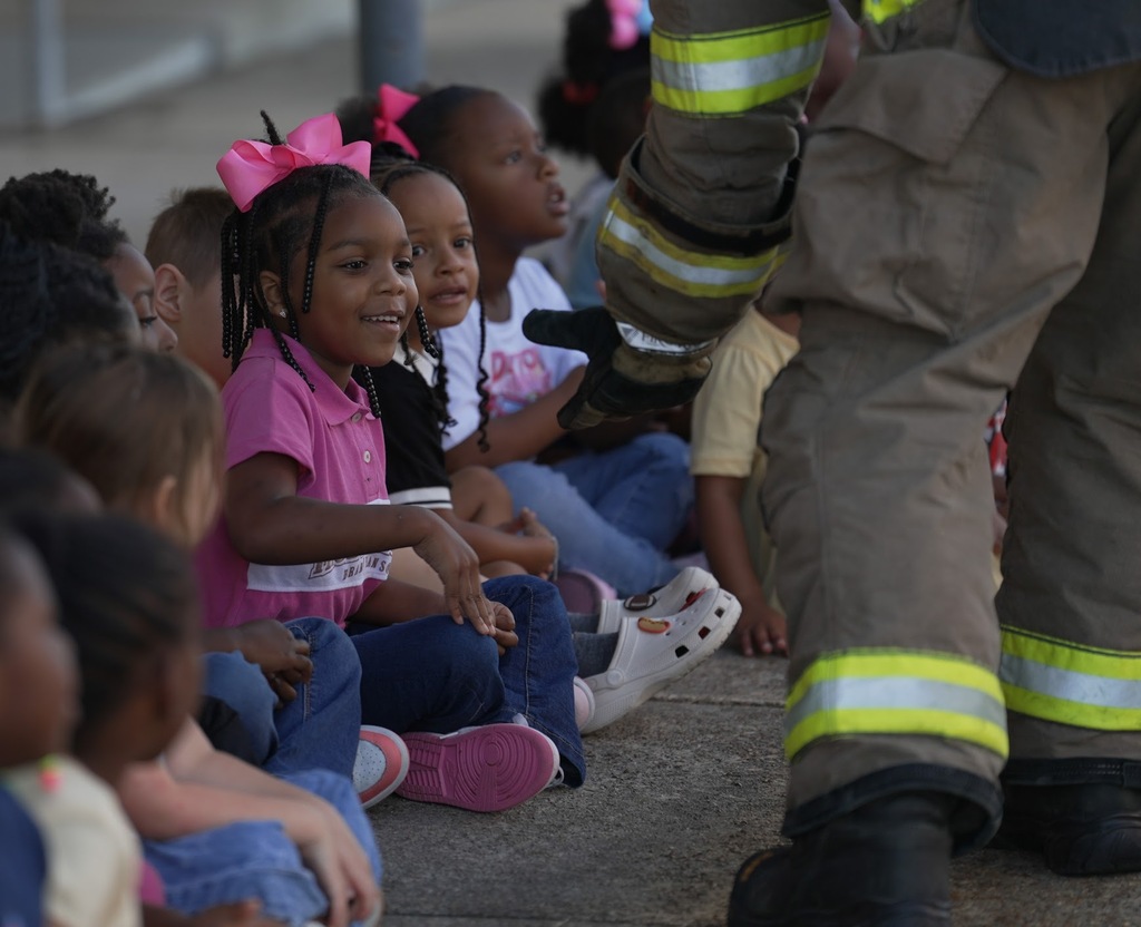 a girl smiling after high-fiving a firefighter in full gear