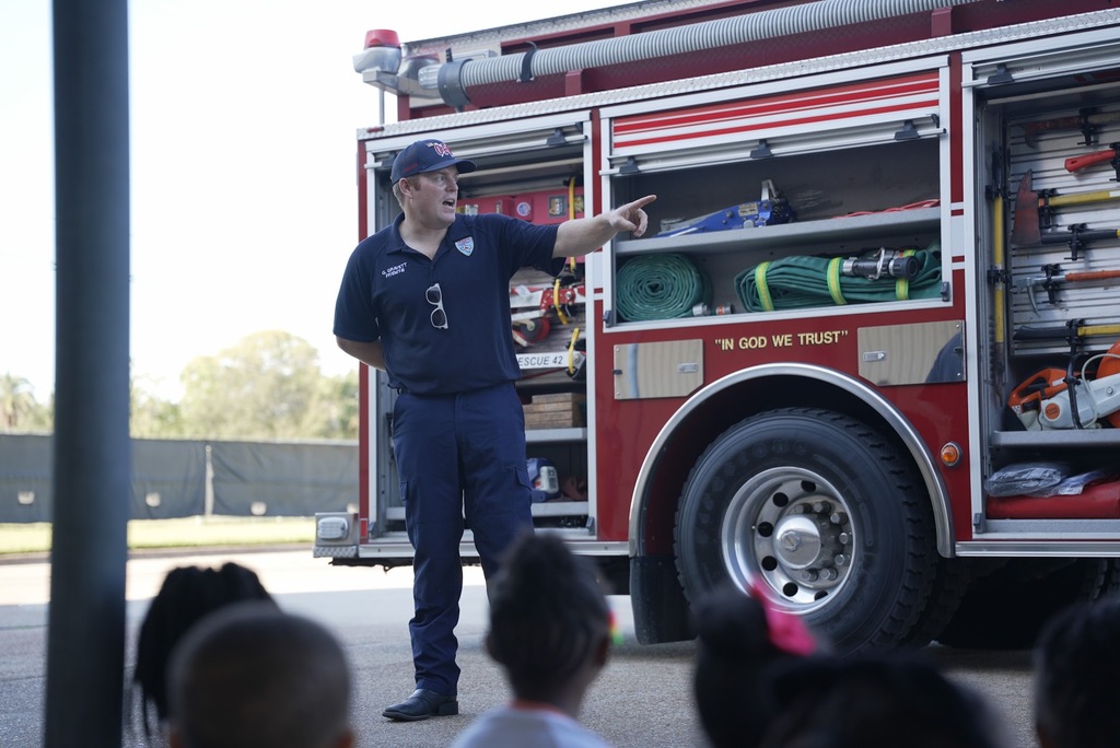 a firefighter talking and pointing in front of a group of children