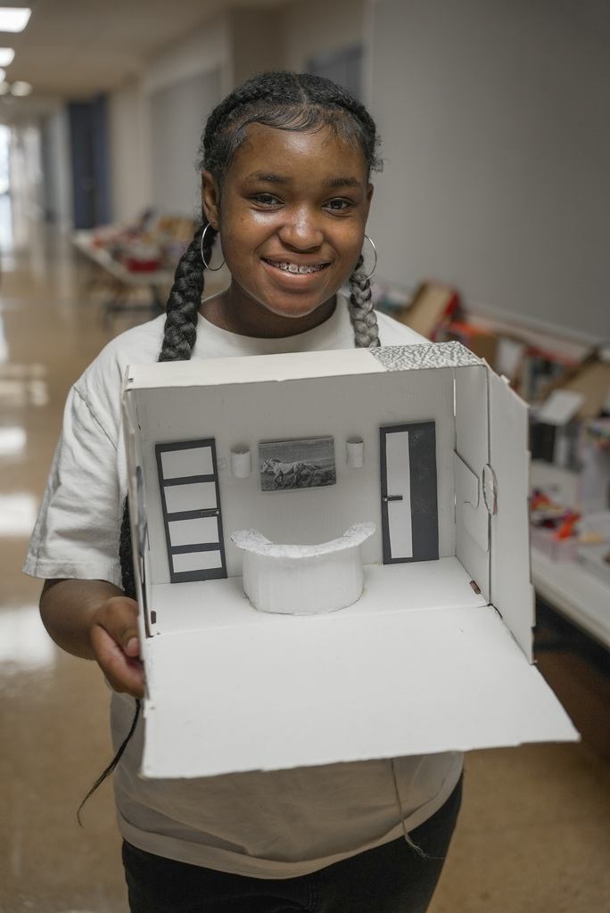 Student holding up a shoebox display of a white room with deak