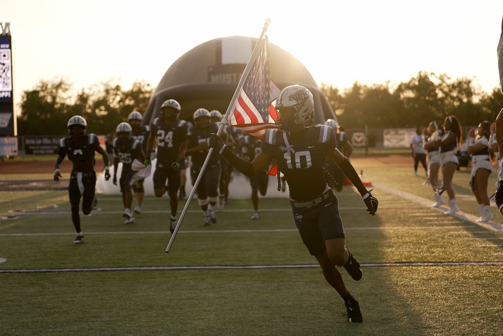 WOS players running out of the helmet, the lead player holds an american flag against the sunset
