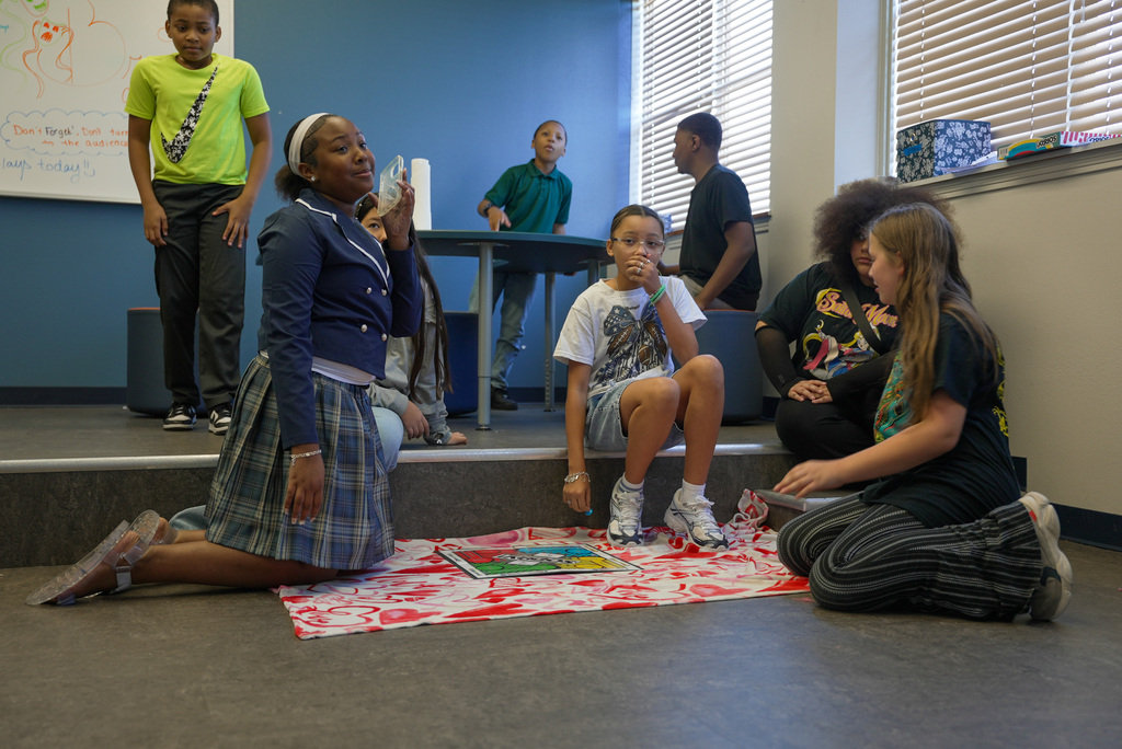 students performing a play sitting around a blanket on the floor