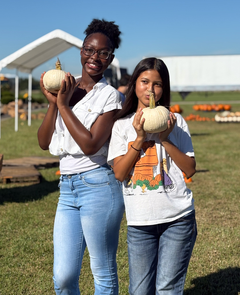 two girls holding up white pumpkins with a pumpkin patch in the background