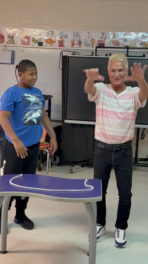 Kevin Spencer holding out his arms next to a student with a piece of string on a table