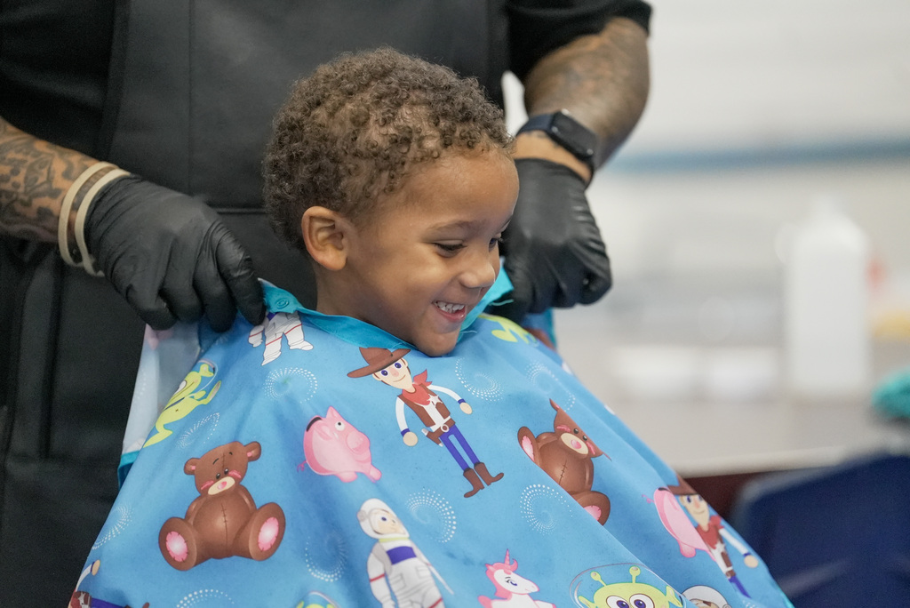 a young boy smiling as a barber puts a cover over him
