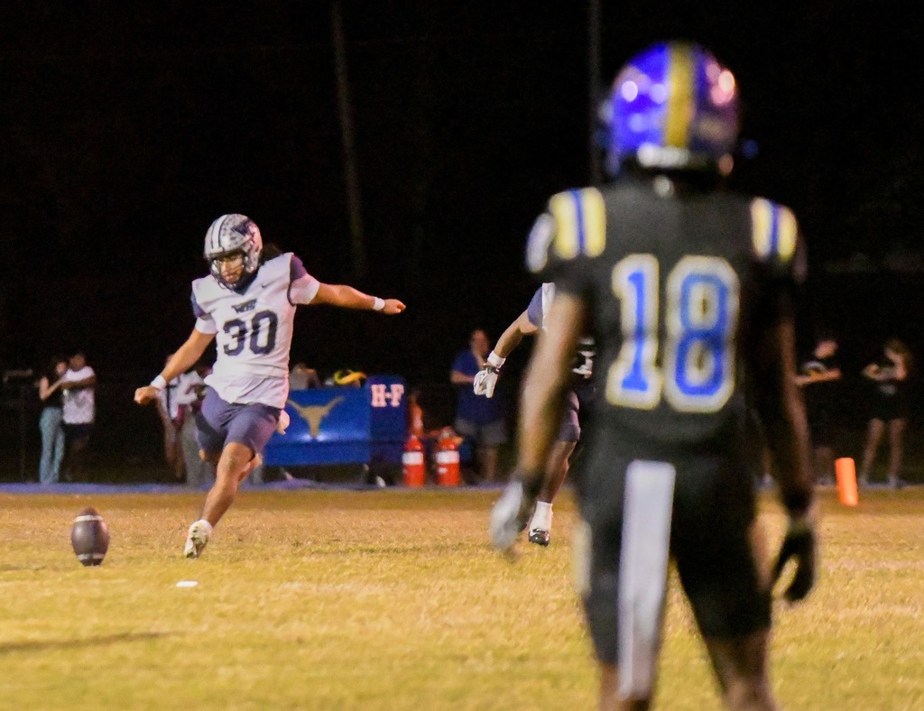 #30 prepares to kick the ball, #18 stands in the foreground blurry