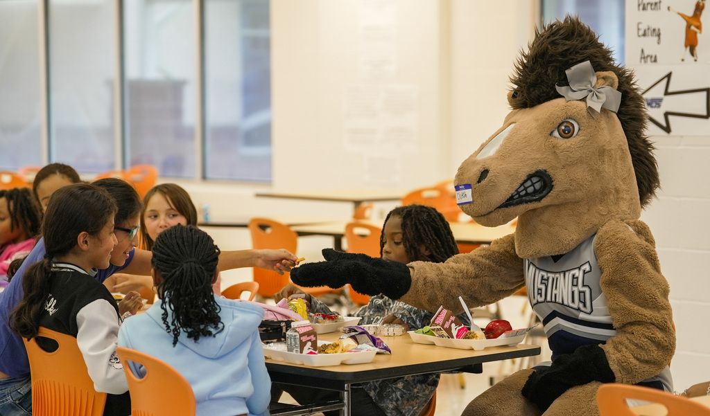 WOSHS Mascot Clutch sitting down with group of children, one reaches out to share a chip