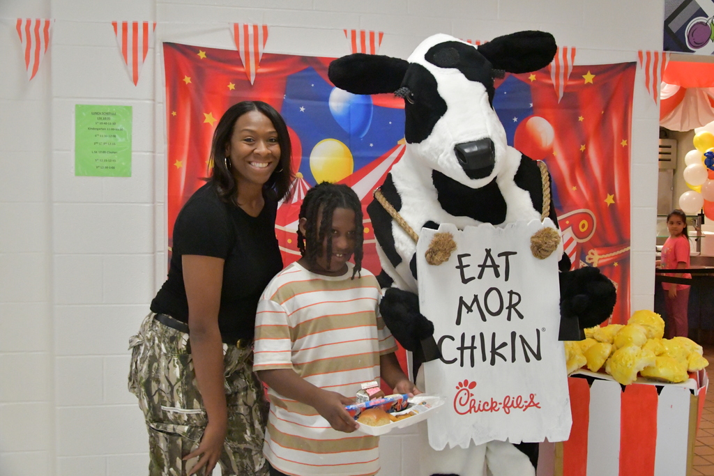 Teacher, student, and Cow mascot taking a picture at lunch