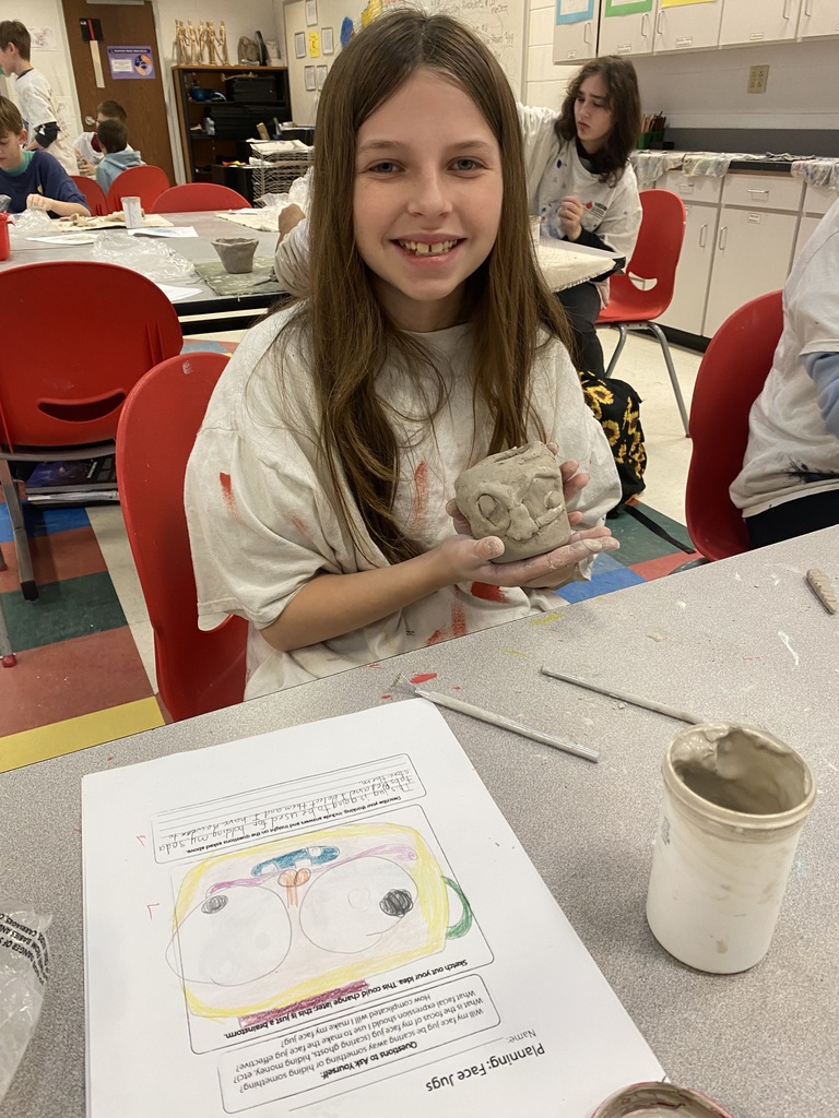6th grade student showing off her clay mask