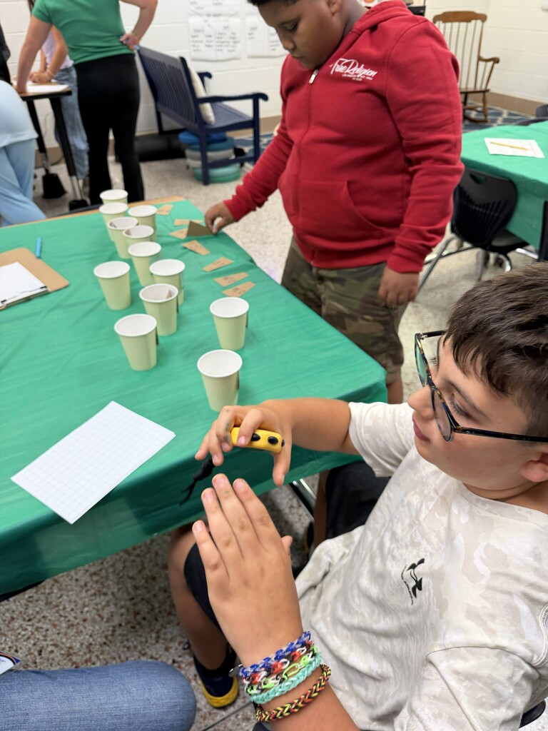 Fifth-grade students participate in Starbucks-themed learning activities, including a book tasting, stem-and-leaf data challenge, coffee bean estimation, and place value games, while enjoying themed snacks and drinks.