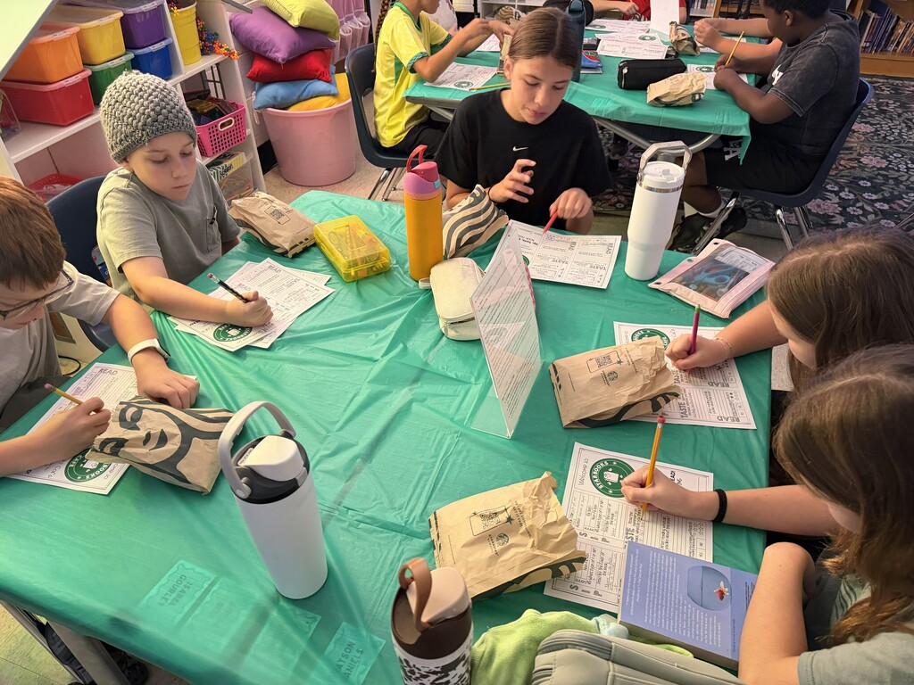 Fifth-grade students participate in Starbucks-themed learning activities, including a book tasting, stem-and-leaf data challenge, coffee bean estimation, and place value games, while enjoying themed snacks and drinks.