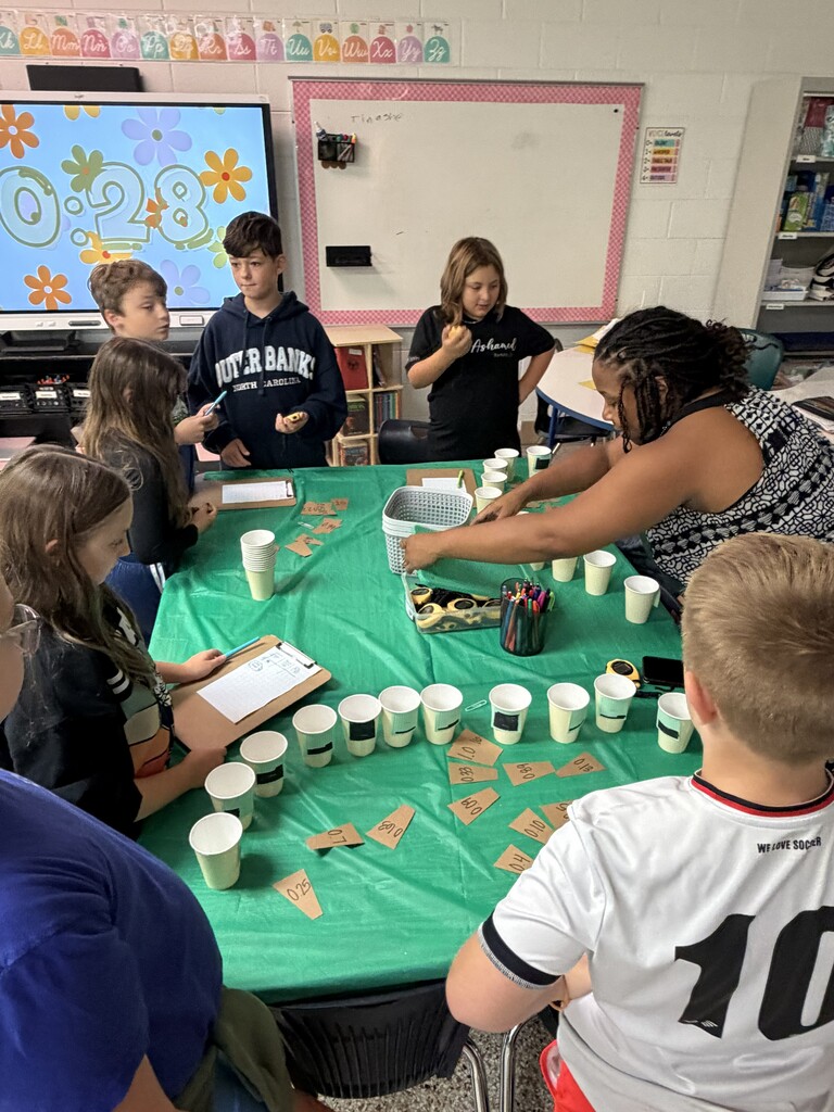 Fifth-grade students participate in Starbucks-themed learning activities, including a book tasting, stem-and-leaf data challenge, coffee bean estimation, and place value games, while enjoying themed snacks and drinks.