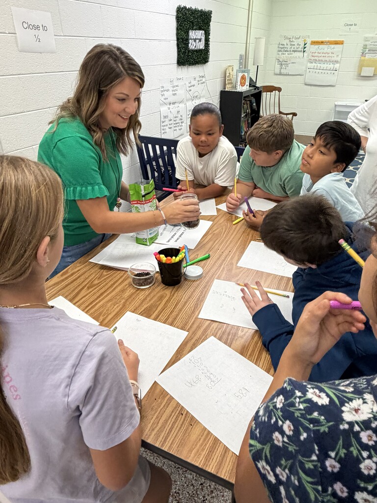 Fifth-grade students participate in Starbucks-themed learning activities, including a book tasting, stem-and-leaf data challenge, coffee bean estimation, and place value games, while enjoying themed snacks and drinks.