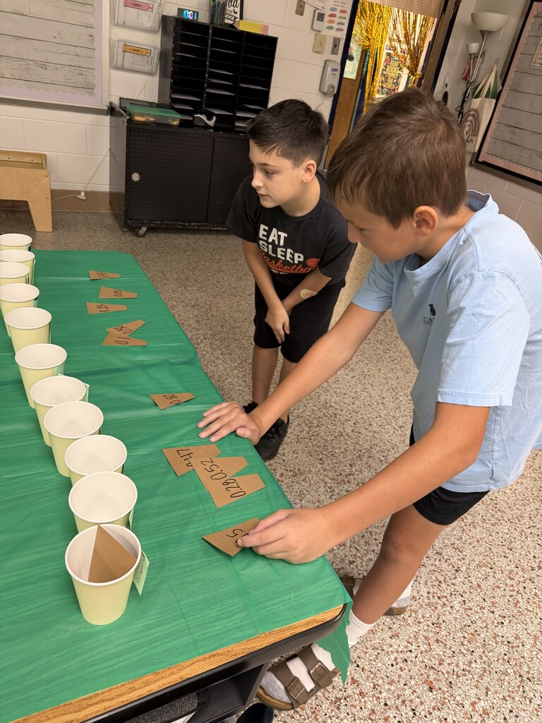 Fifth-grade students participate in Starbucks-themed learning activities, including a book tasting, stem-and-leaf data challenge, coffee bean estimation, and place value games, while enjoying themed snacks and drinks.