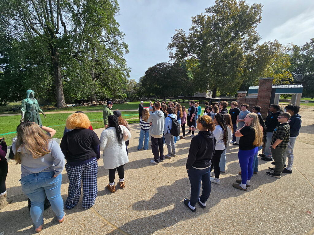 Students standing and listening to Mr. Mark Summers an author and historian who serves as the Educational Director of Youth and Public Programs for Jamestown Rediscovery in front of the Pocahontas Statue