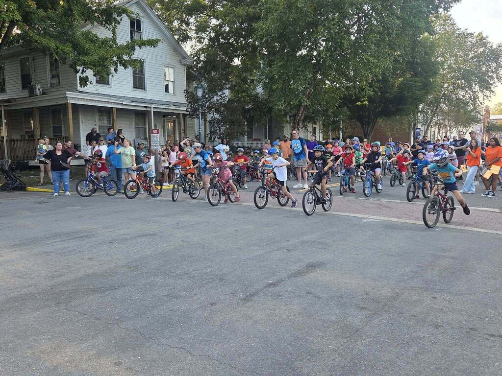 Young Pointer students ride their bicycles during the Tour de Crab community event, smiling and enjoying the ride.